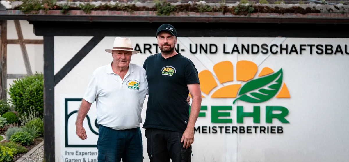 Marcel Fehr mit seinem Vater vor dem Firmenschild von Fehr Garten- und Landschaftsbau in Oberstdorf