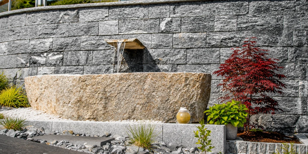 Wandbrunnen aus Naturstein mit Wasserauslauf und Granittrog