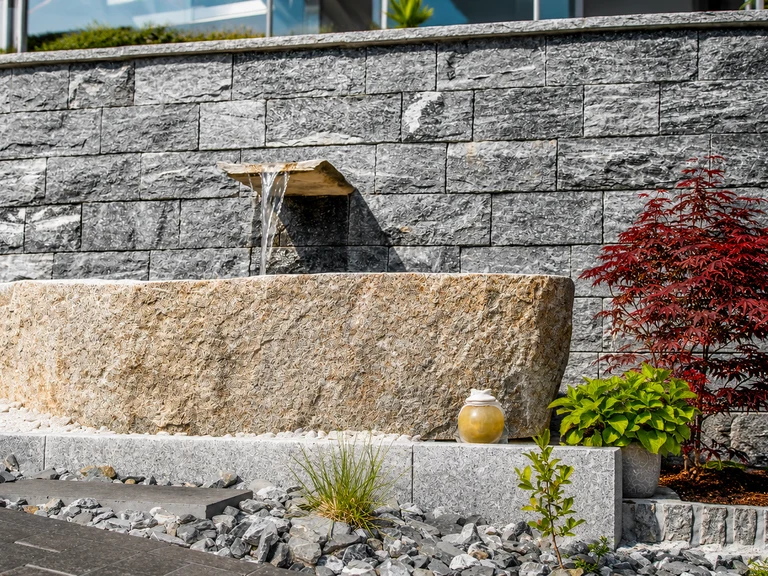 Gartenbrunnen aus Naturstein mit Granittrog und plätscherndem Wasserauslauf