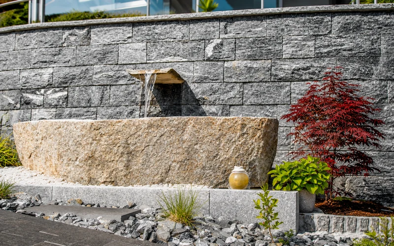 Gartenbrunnen aus Naturstein mit Granittrog und plätscherndem Wasserauslauf